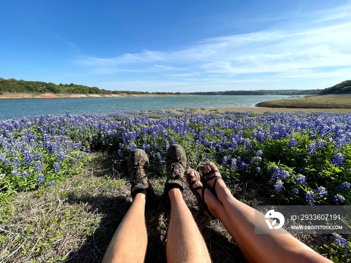 Sitting in a field of Texas bluebonnets overlooking lake, two people sit in field of wildflowers