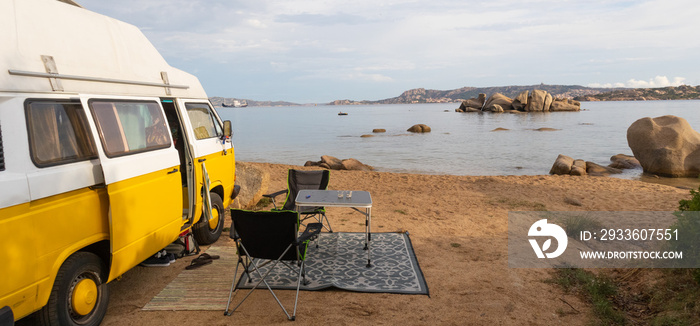 Tourism vacation and travel. Old colorful retro camper van on camping site at beautiful rocky coastal landscape of Costa Smeralda, north east Sardinia, Italy.