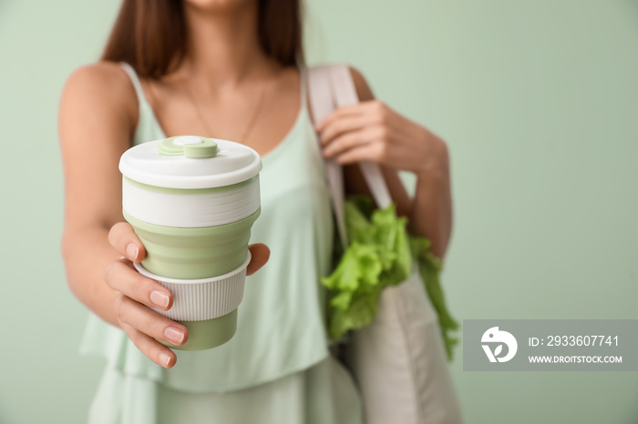 Young woman with eco bag and cup of coffee on green background, closeup