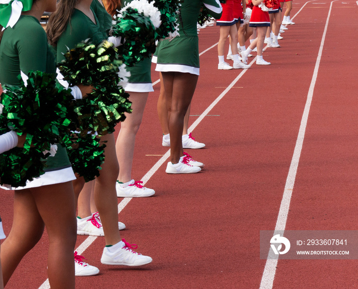 Two teams of cheerleaders standing on the tsideling cheering during football game