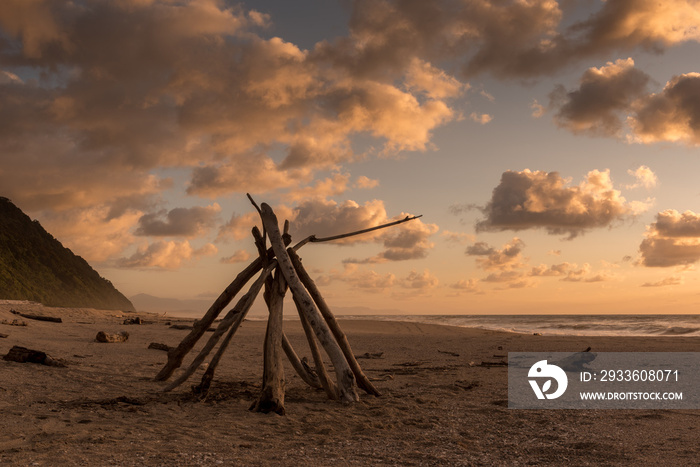 Pyramid of driftwood on the beach at sunset at the end of the Heaphy Track, Tasman, New Zealand.