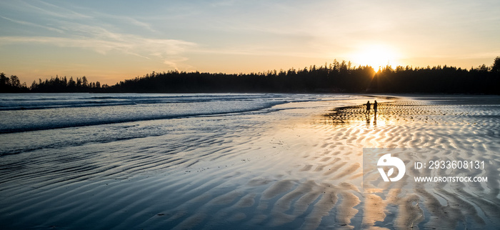 Two people walking along a beach at sunset in Tofino, British Columbia