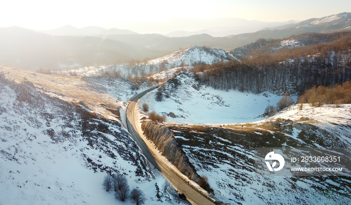 Amazing sunset aerial top drone view of high-speed road between the picturesque mountains in winter. Top down view of picturesque mountain serpentine stretching into the distance.