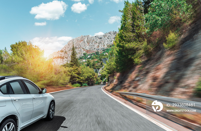 White car moves on the road among the mountains and forests.