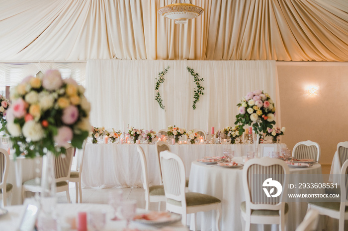 Coziness and style. Modern event design. Table setting at wedding reception. Floral compositions with beautiful flowers and greenery, candles, laying and plates on decorated table.