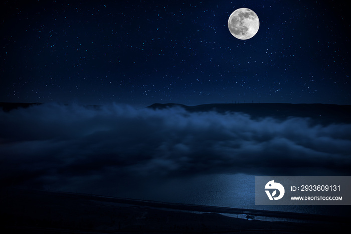 This dramatic moon rise in a deep blue night time sky is accented by highlighted clouds and beautiful, calm lake reflection.Selective focus