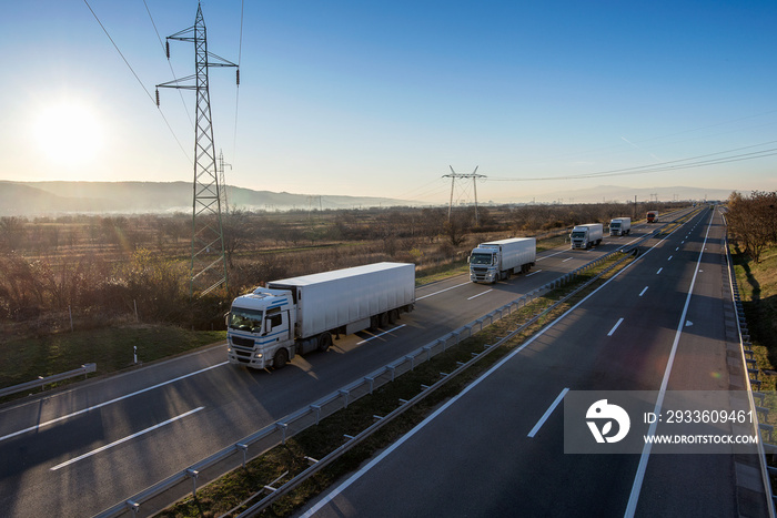 Fleet or Convoy of big transportation trucks in line on a countryside highway under a blue sky.