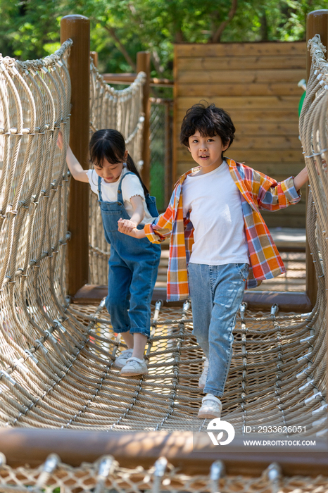 两个小孩子相互鼓励牵手走绳桥