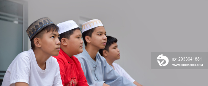 Portrait asian muslim or islamic boys sitting with muslim boys in a row to pray or to do the religious activity, soft and selective focus.