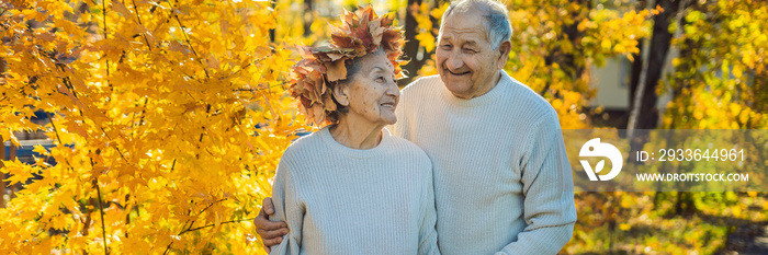 Happy old couple having fun at autumn park. Elderly man wearing a wreath of autumn leaves to his elderly wife BANNER, LONG FORMAT