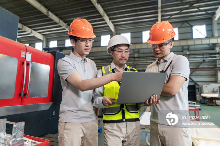 三个工程师穿保护工作服戴着安全帽在工厂工作