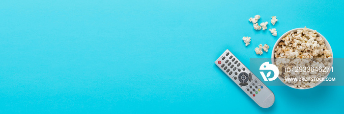 Bowl with popcorn and remote control for TV on a blue background