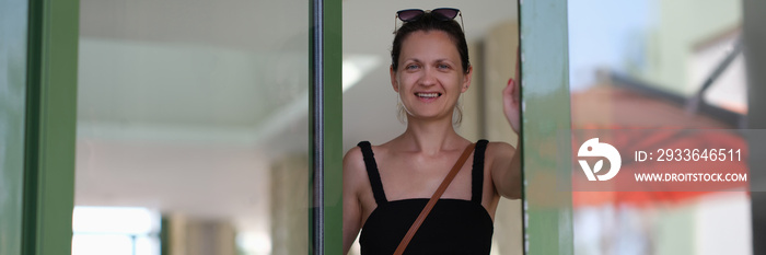 Beautiful smiling young woman opens glass door