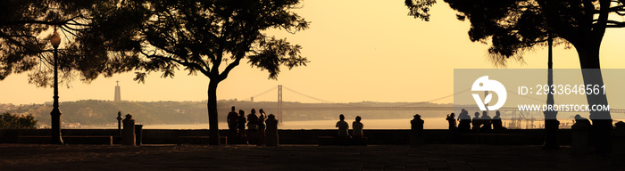 Beautiful panoramic image of silhouettes looking at the Ponte 25 de Abril bridge and the Sanctuary of Christ the King (Cristo Rei) at sunset from the Sao Jorge Castle in Lisbon, Portugal