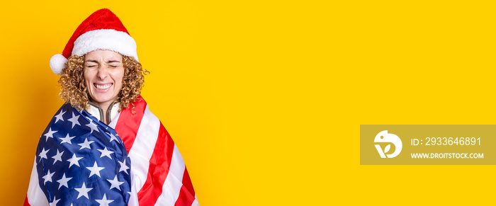 Young woman squinting in santa claus hat with usa flag on yellow background. Banner.