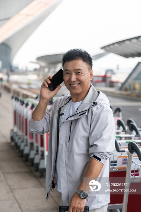 老年男人在机场拉着行李箱打电话