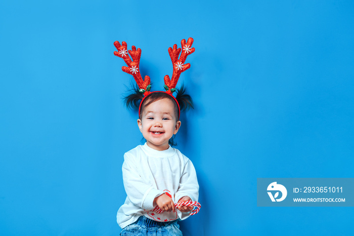 Little funny girl in red toy antler on head ready and happy for christmas holidays, on blue backgrou