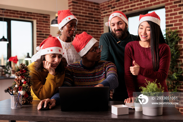 Multiethnic team of people using laptop in festive office, working on startup business during christ