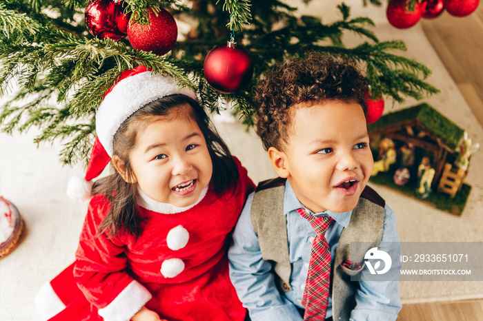 Group of two adorable 3 year old kids playing by the Christmas tree, top view