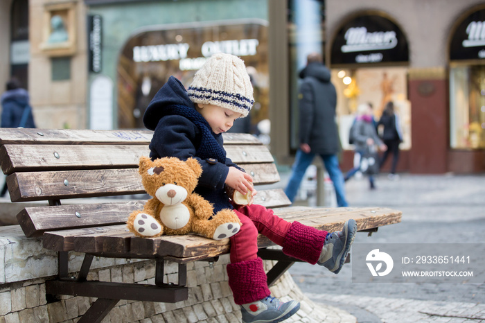 Fashion toddler boy with teddy bear toy, eating traditional Czech sweet pastry, called trdlo in the 