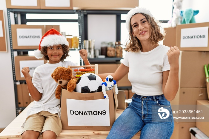 Young mother with little son wearing christmas hat at donations stand screaming proud, celebrating v