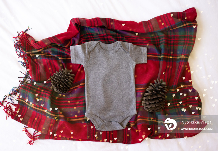 Gray blank newborn baby bodysuit on a tartan/plaid Christmas background with pine cone props