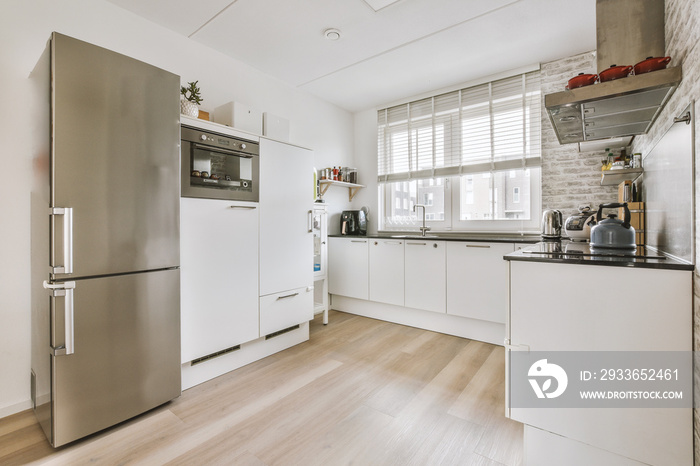 Interior of light kitchen and dining room with balcony doors in contemporary apartment at daytime