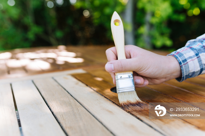 young woman painting wooden exotic wood table in the garden with a brush