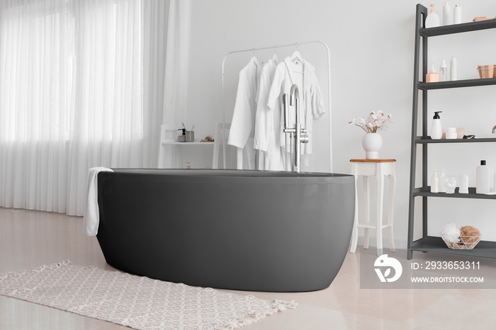 Interior of stylish bathroom with black bathtub and shelf unit