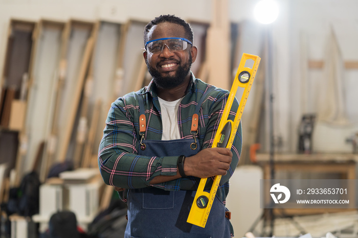 Portrait of African American male carpenter holding precision level making new furniture at wood wor