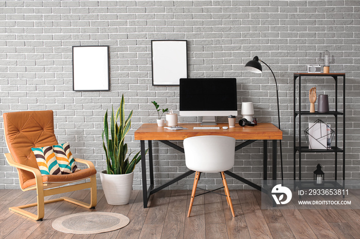 Interior of stylish room with modern workplace and blank photo frames on grey brick wall