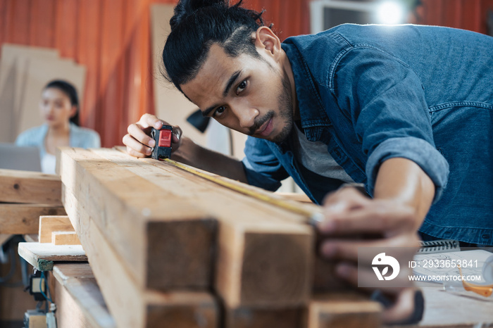 Young Asian man Carpenter uses a tape measure to measure wood on the workbench in woodcraft carpentr