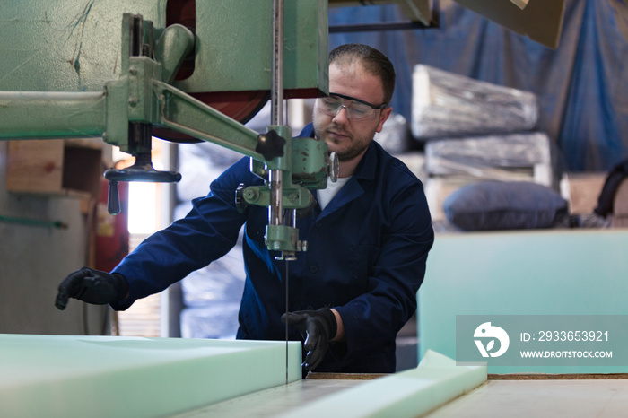 Young man in a furniture factory is cutting the foam for the sofa
