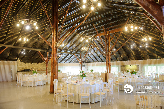 close up photo of the interior of a wedding restaurant: arranged round white tables and wooden pilla