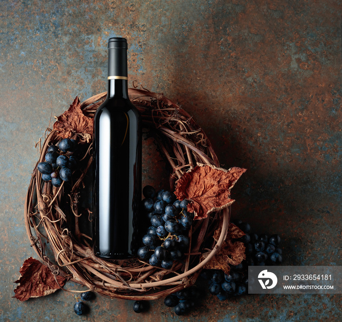 Bottle of red wine with grapes and dried vine leaves on an old rusty background.