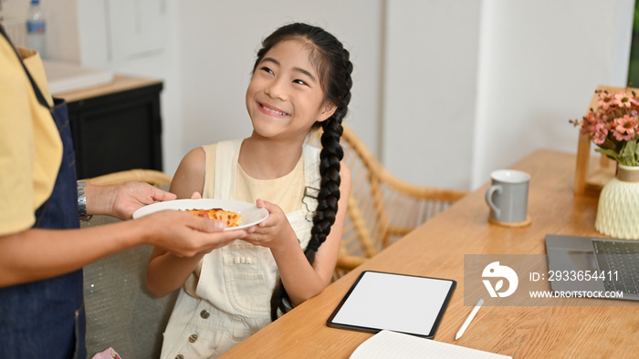 Mom gives bread to her daughter while she studies online.