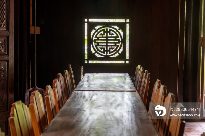 Wooden tables and chairs opposite a carved window with sunlight at a Buddhist temple, Da Nang, Vietn