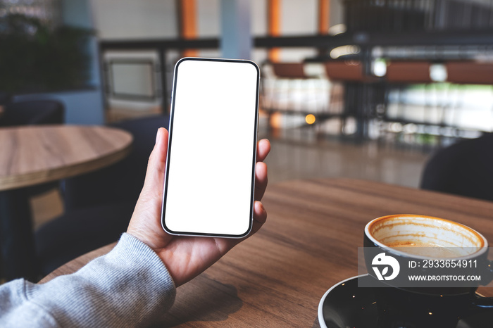 Mockup image of hands holding mobile phone with blank desktop screen in cafe