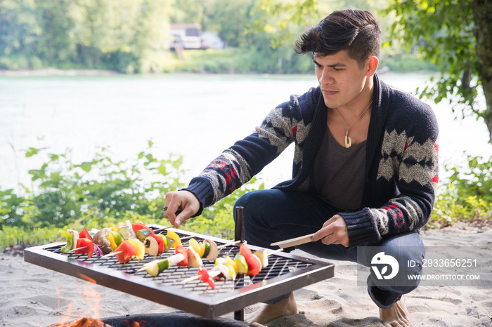 Man cooks vegetable kebab over fire pit