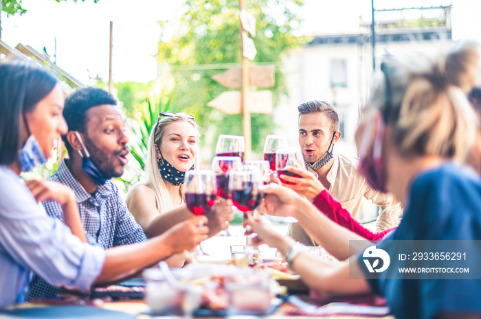 Friends toasting red wine at outdoor restaurant bar with face mask down - New normal lifestyle conce