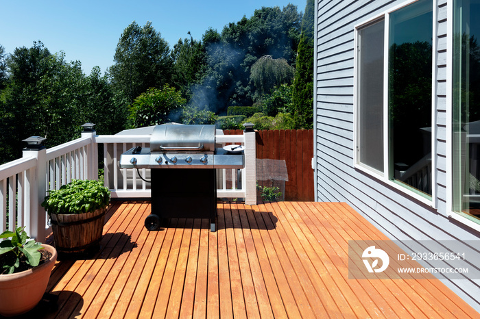 Large outdoor BBQ cooker with smoke coming out while on home wooden deck