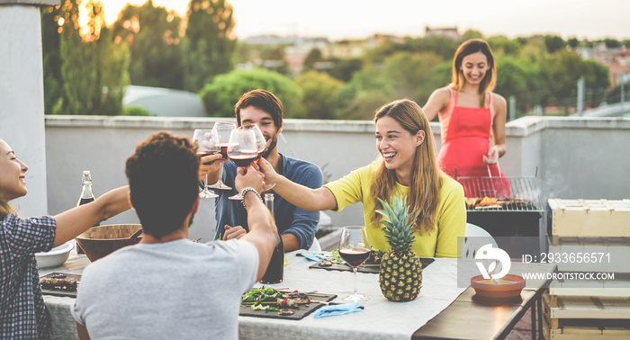 Young friends cheering with red wine at rooftop barbecue dinner - Happy people doing bbq dinner outd