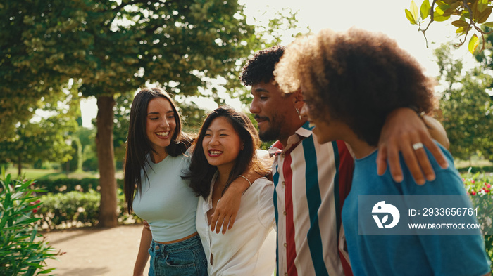 Happy multiethnic young people walk embracing on summer day outdoors. Group of friends are talking a