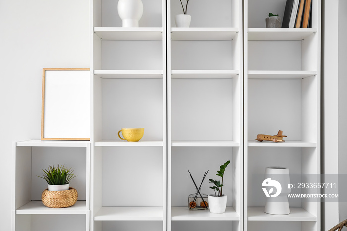 Big shelving unit with decor and blank frame near light wall