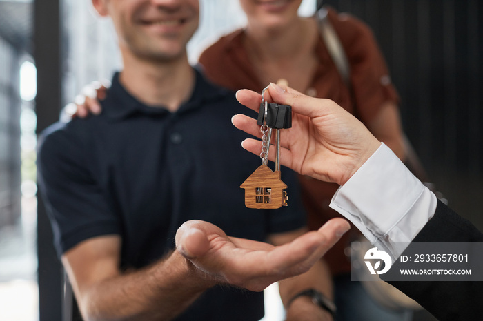 Close up of real estate agent giving keys to couple with focus on house keychain, copy space