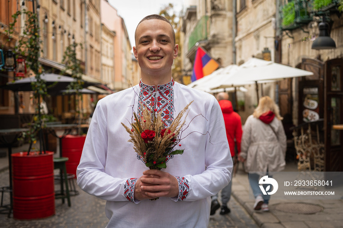 Portrait of a happy handsome young man in traditional Ukrainian embroidery on a city street. A succe