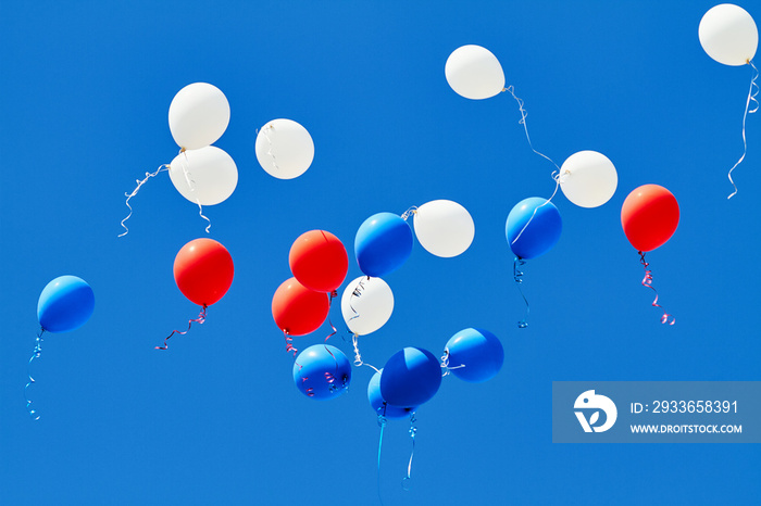 Multicolored helium balloons flying up in the blue sky