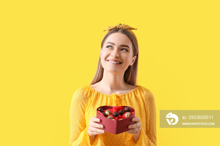 Happy young woman with delicious chocolate candies in box on color background