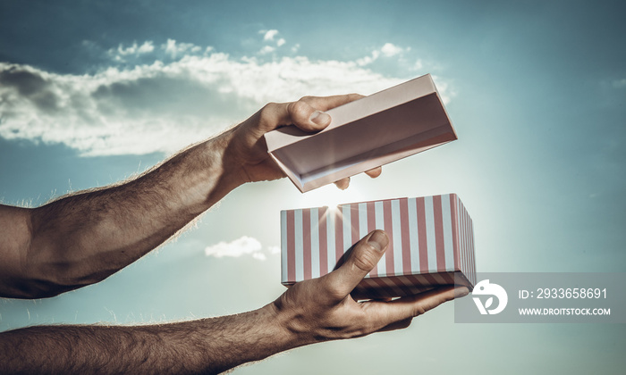 Male hand showing pink gift box with blue sky background. Valentines day concept. Small Handmade gif