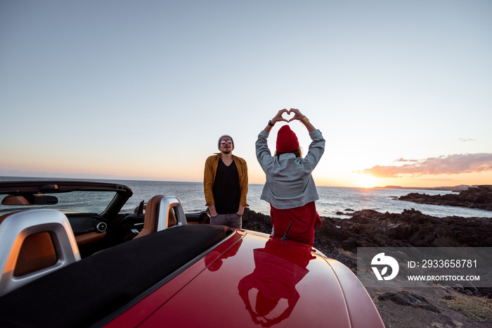 Couple enjoying beautiful views on the ocean, standing together near the car on the rocky coast, sho